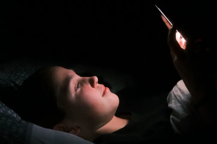 Personne allongée dans son lit, le visage éclairé par un téléphone