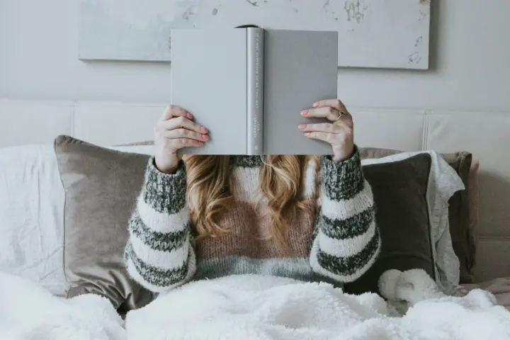 Femme assise dans son lit avec un livre ouvert