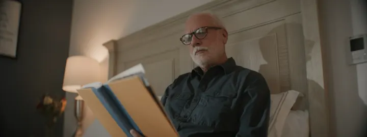 Homme âgé portant des lunettes et lisant dans son lit